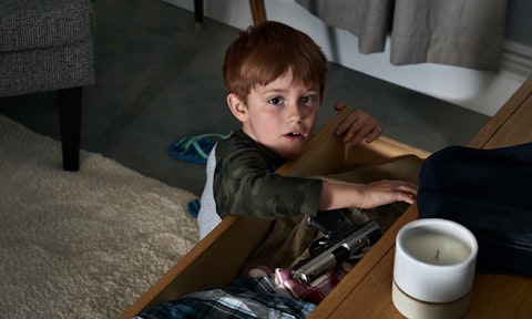 Young boy searching in open drawer for an unsecured gun among clothes