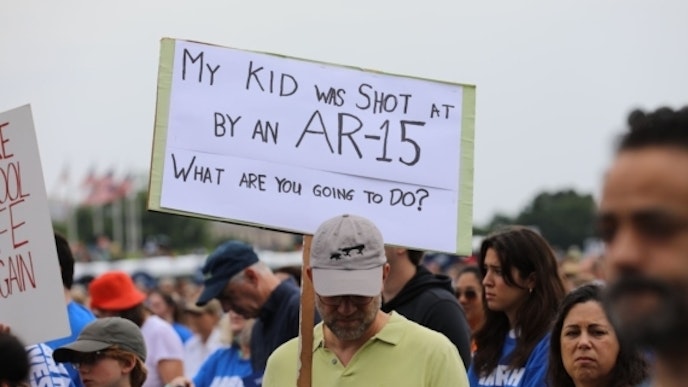 Survivor at the March for our lives 2022 rally holds up a sign stating my kid was shot by an ar 15